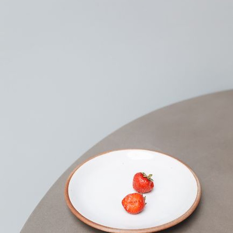 Two strawberries elegantly placed on a simple ceramic plate against a soft background.