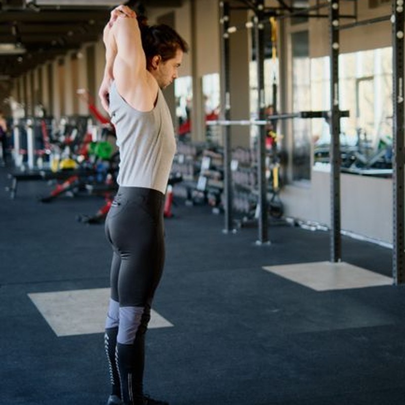 Caucasian male doing stretching exercises in an indoor fitness gym with modern equipment.