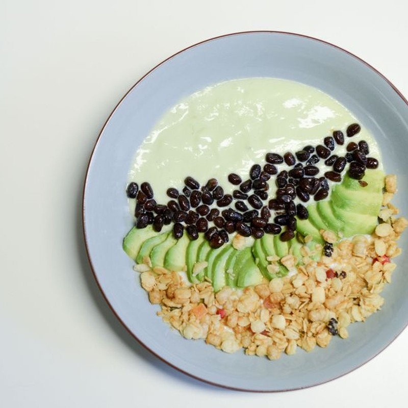 A healthy smoothie bowl featuring avocado, black beans, and granola served in a ceramic bowl.