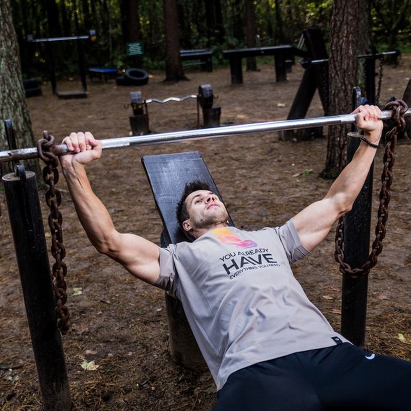 Man weightlifting outdoors, using a bench press setup amid trees for strength training.