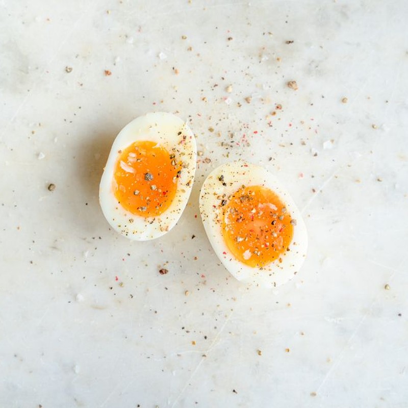 Top view of halved soft boiled egg placed on marble table and spiced with salt and pepper