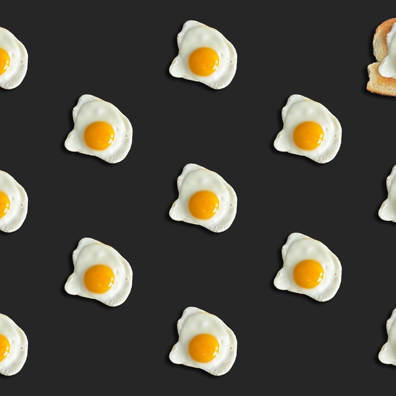 Creative pattern of fried eggs on black with toast, top view.