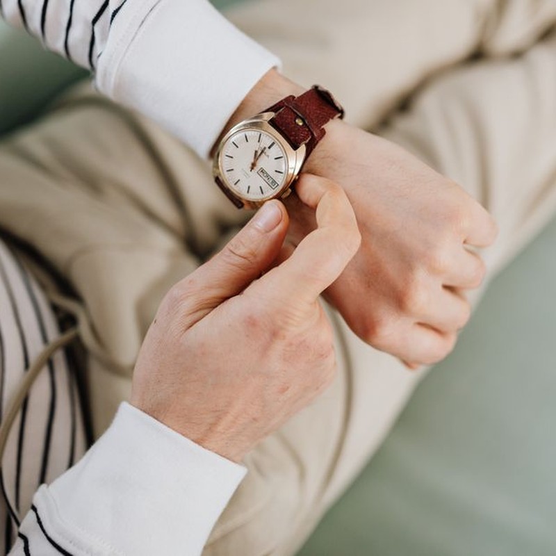 A person adjusts an analog wristwatch with a leather strap, showcasing style and precision.