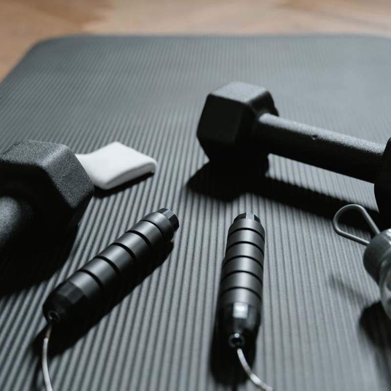 Close-up of dumbbells, jump rope, and water bottle on a yoga mat, ideal for home fitness routines.