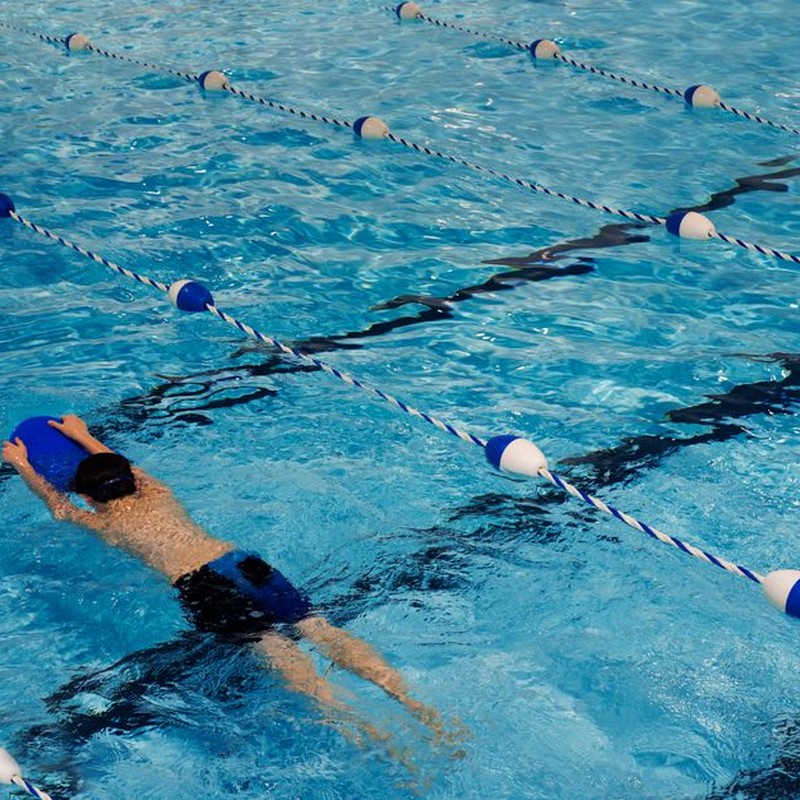 A young swimmer practicing with a kickboard in a swimming pool on a sunny day.