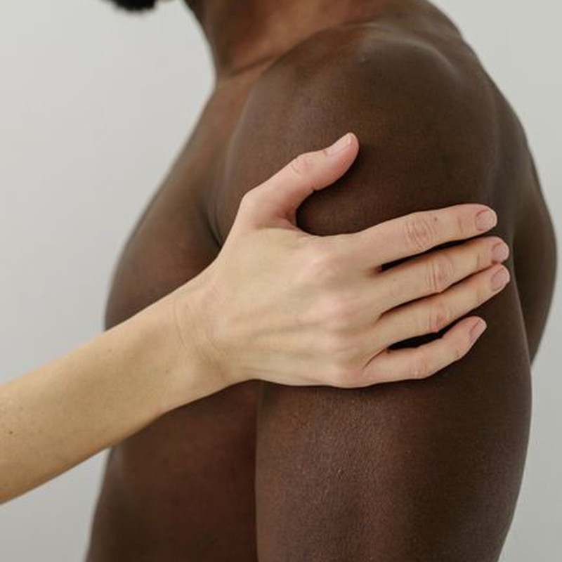 A close-up view of a hand resting on a muscular shoulder, displaying a sense of touch and connection.