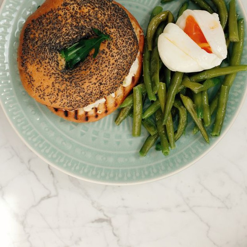 Ceramic plate with tasty fresh bagel and asparagus with poached egg served on white marble table in light modern kitchen at home