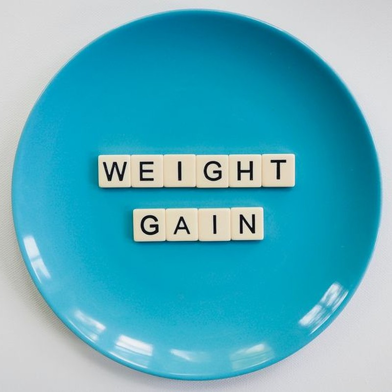 Scrabble tiles spelling 'weight gain' on a blue plate, symbolizing health and diet.